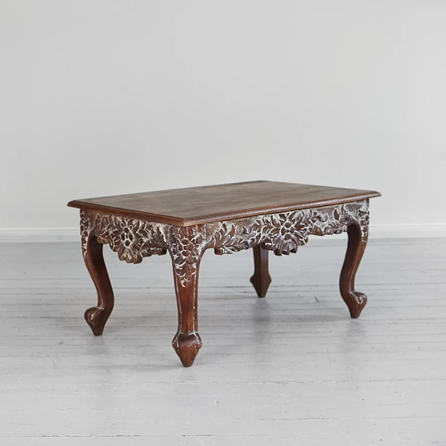 Ornate carved wood coffee table with scrolled feet and vine detailing.