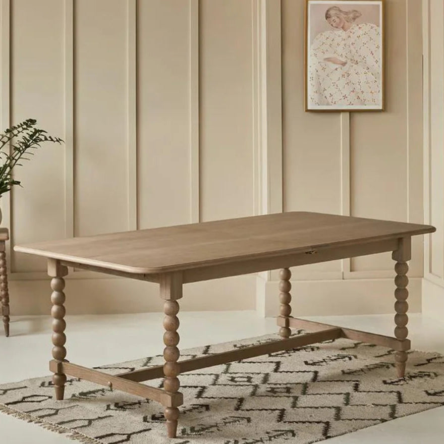 Wooden dining table in a room with beige paneling and a decorative rug.