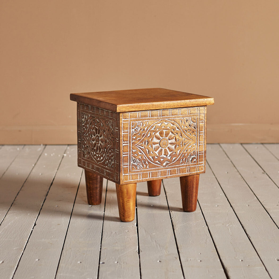 Wooden side table with intricate carvings on a wooden floor.