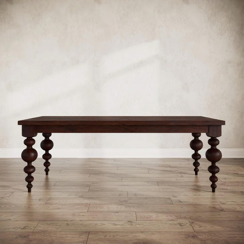 Wooden dining table with turned legs on a wooden floor against a beige wall.