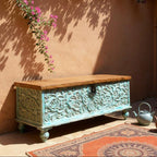 Decorative wooden chest with floral patterns against a warm-toned wall with pink flowers.