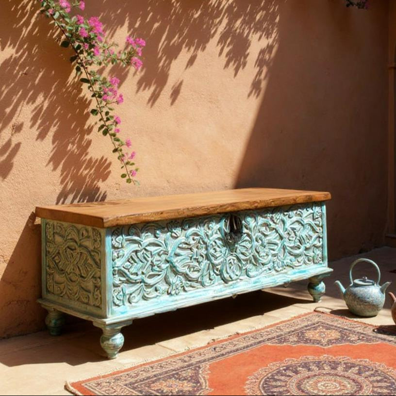 Decorative wooden chest with floral patterns against a warm-toned wall with pink flowers.